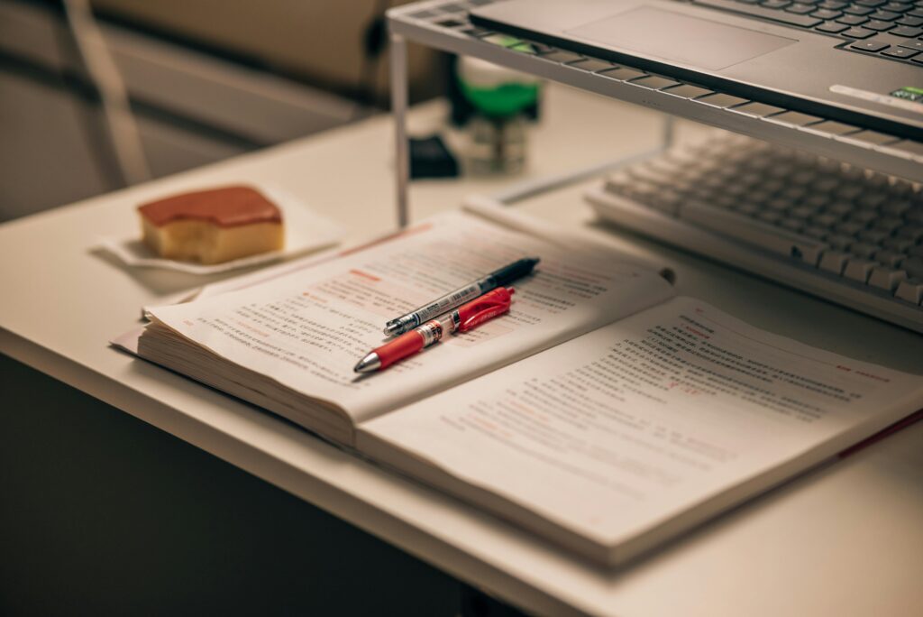 Open book with study notes, pens, and a laptop on a desk creating a focused study environment.